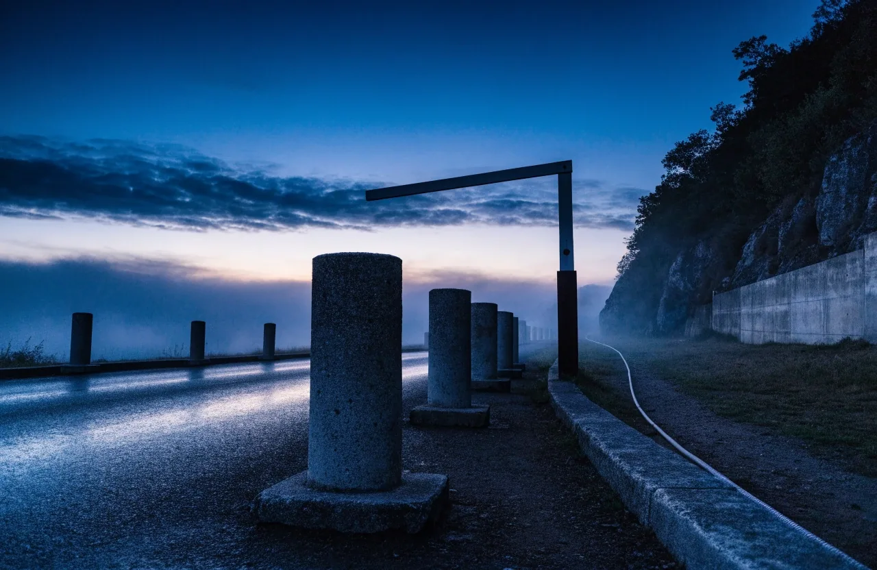Utility poles carrying fiber receding along a fogged valley road at dusk