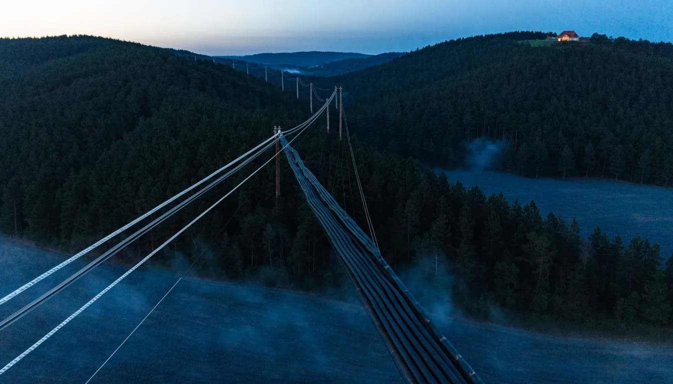 An aerial cable trunk running toward a lit house on a ridge at dusk