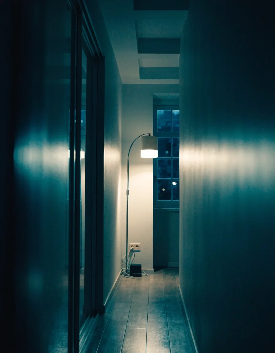 Apartment room at night with a lamp by the window and a router resting on the floor near the wall outlet