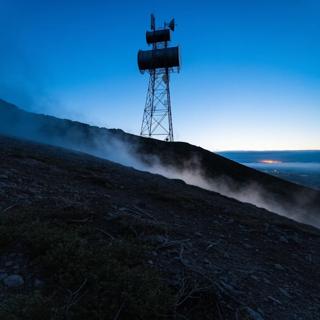 An antenna array on a fogged hill at dusk above a hidden valley